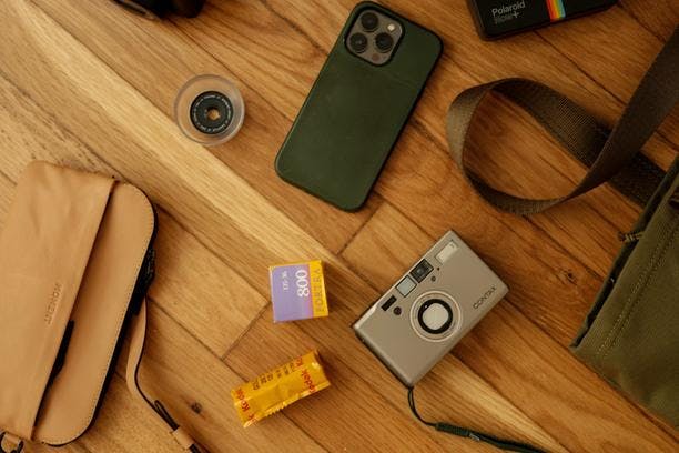 A flatlay image of a Contax T3, sunglasses, Moment lenses, and a green tote.