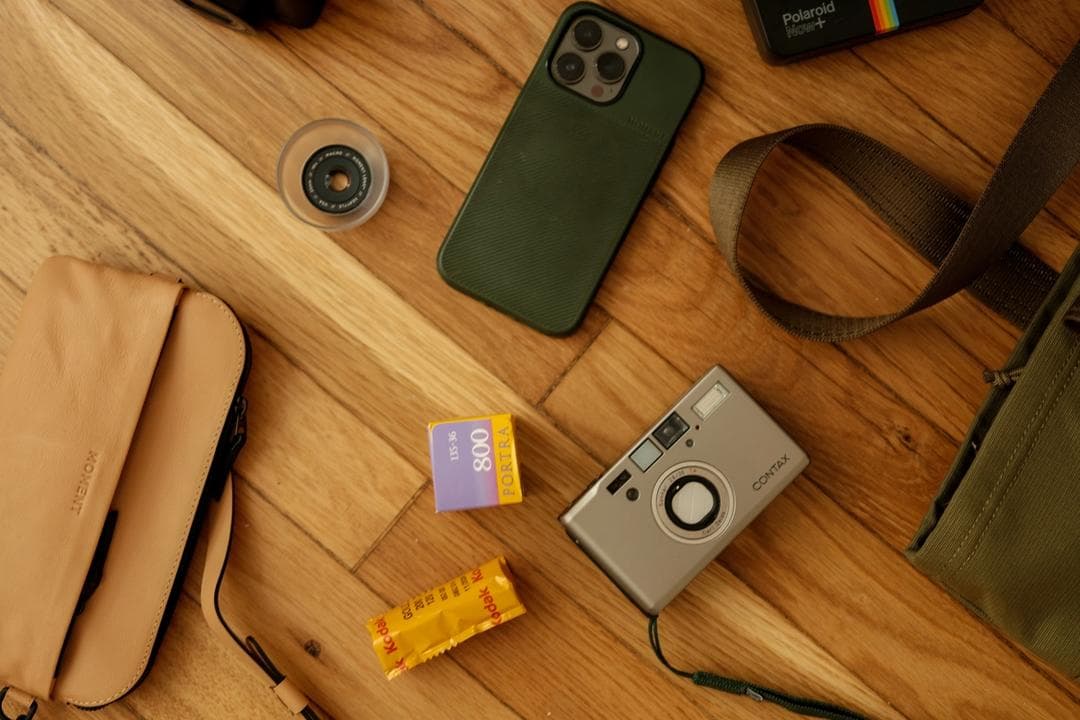 A flatlay image of a Contax T3, sunglasses, Moment lenses, and a green tote.