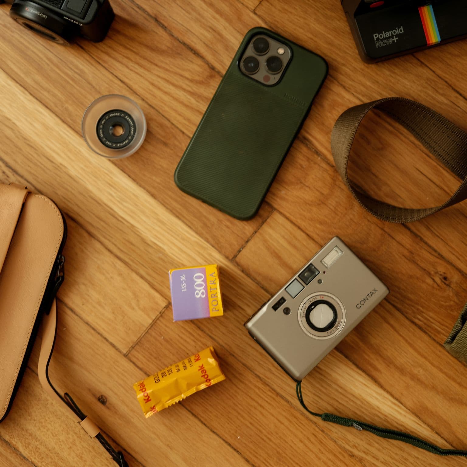 A flatlay image of a Contax T3, sunglasses, Moment lenses, and a green tote.