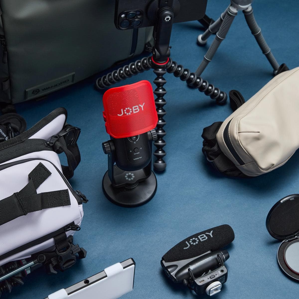 Tons of mobile gear and a loud jOBY mic on a flat lay gear image with a blue background.