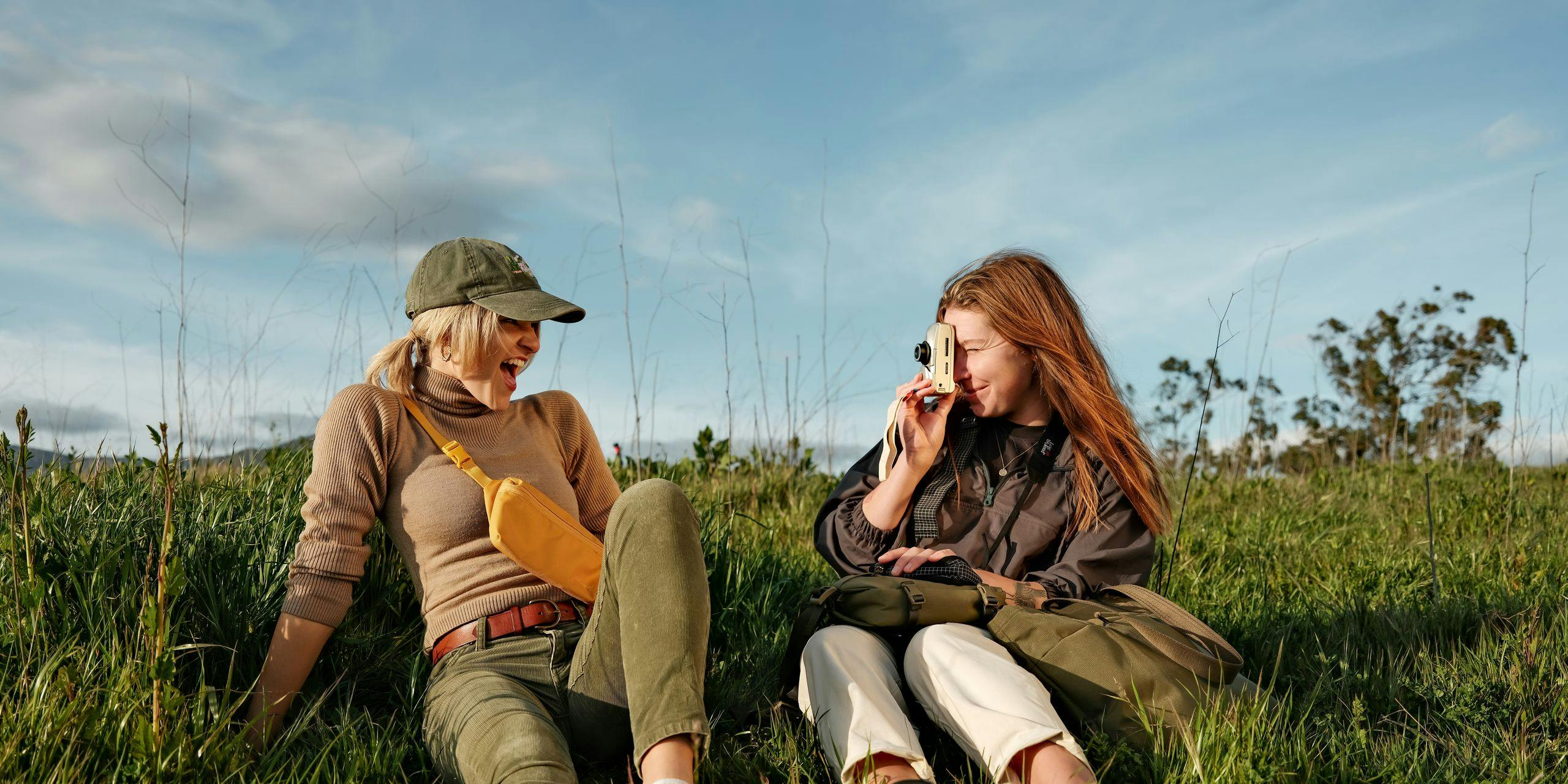 Two girls laughing and taking pictures in a field with Moment Bags.