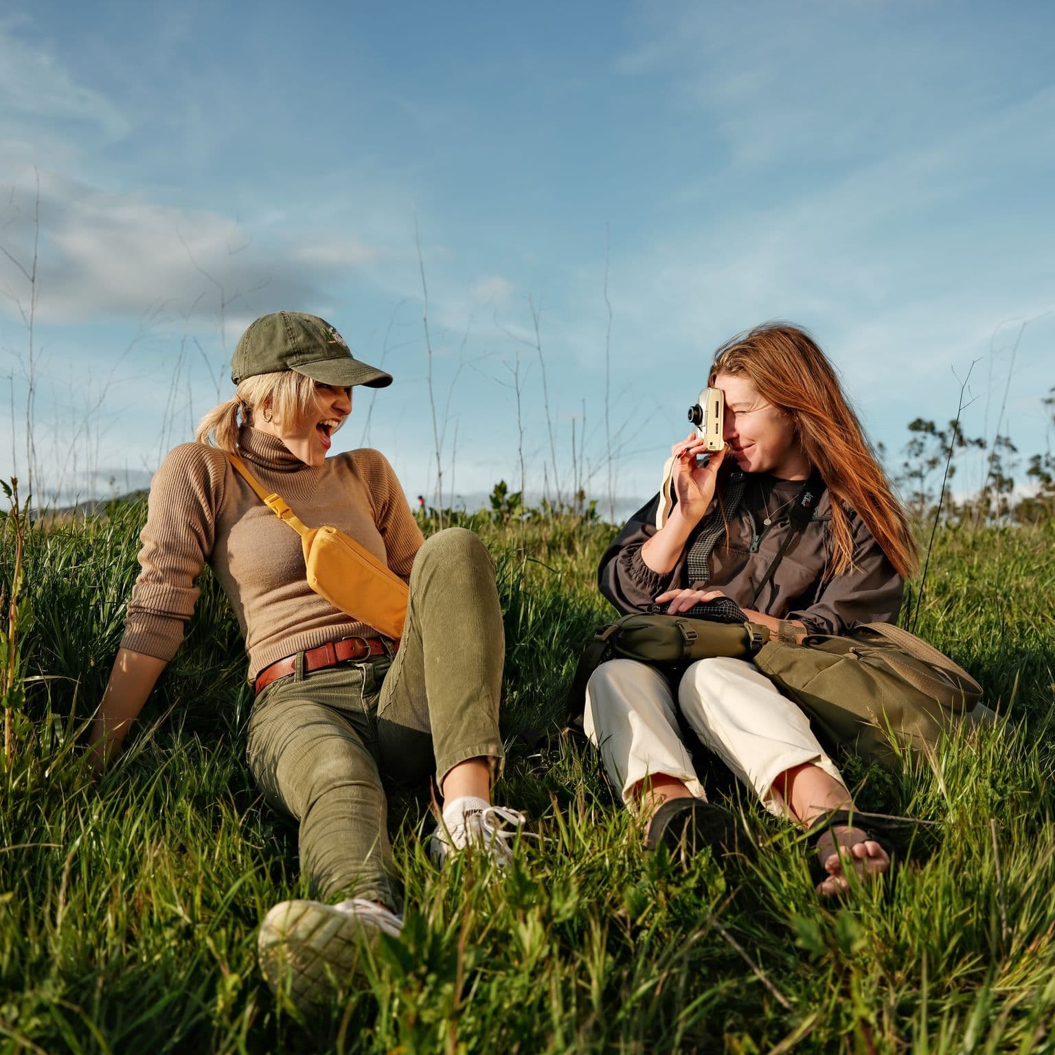 Two girls laughing and taking pictures in a field with Moment Bags.